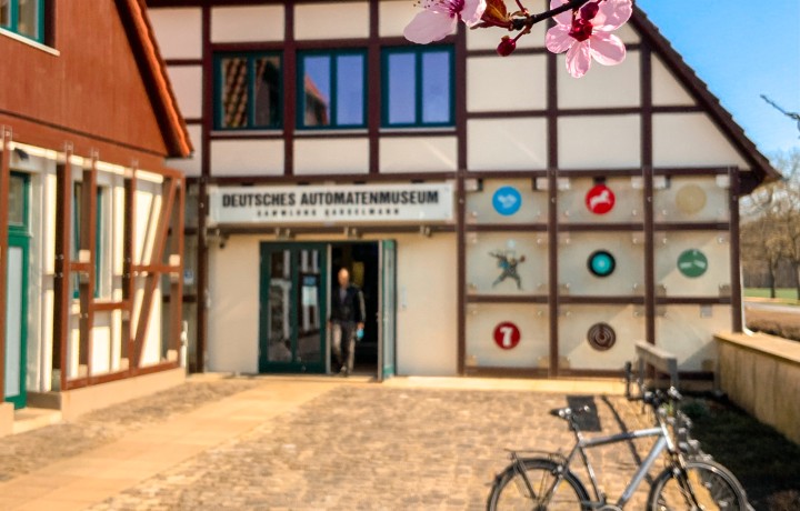 Automatenmuseum Außenansicht bei geöffneter Tür im Frühling mit Blüten im Vordergrund