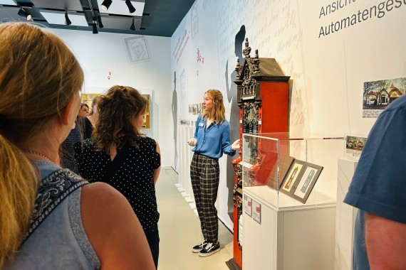 Blick über die Schulter einer Führungsteilnehmerin. Die gruppe bildet eine Halbkreis um die Führungsperson, die die Schokoladenautomaten Rhenania erklärt.