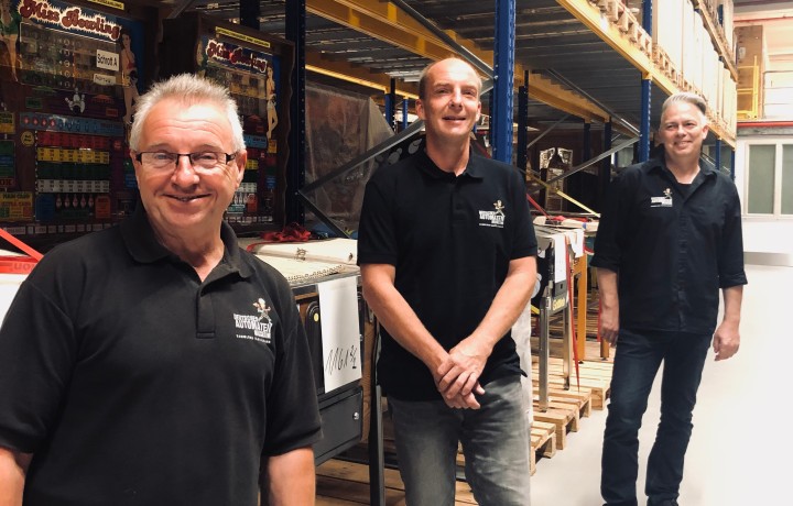 Die drei Techniker der Museumswerkstatt stehen im Depot vor einer Reihe von Flipper-Automaten.