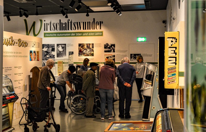 Eine Gruppe von Menschen, darunter Personen mit Gehilfe und Rollstuhl bilden eine Halbkreis um eine Musikbox