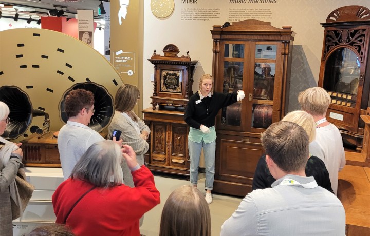 Eine Gruppe von Menschen schaut auf mechanischen Musikautomaten, welche von einer Führungsperson erklärt werden.